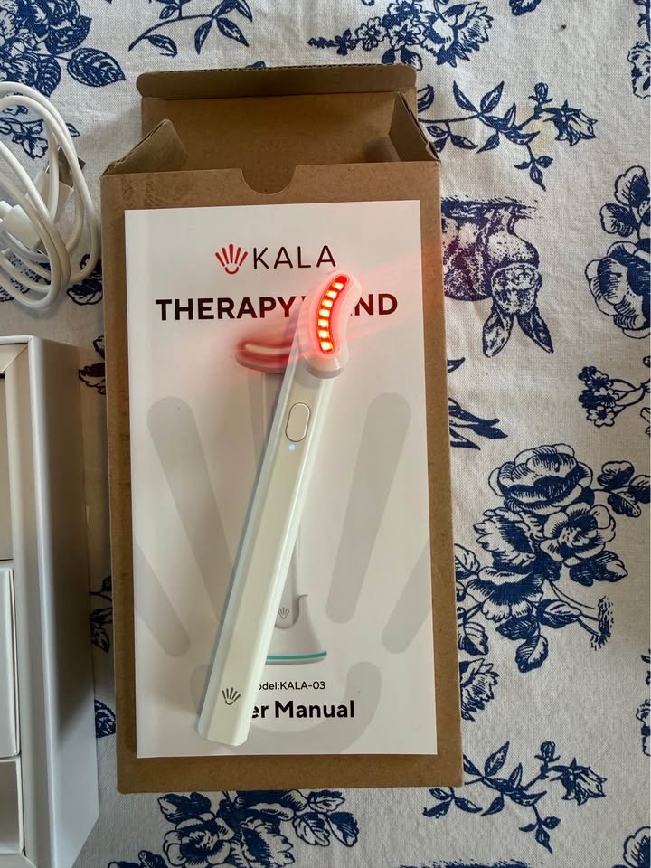 Kala Therapy Wand with active red light LEDs glowing on user manual